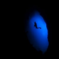 Силуетът на водолаз със светлината на гмуркане изследва пещера в Раджа Ампат, Индонезия. Печат на плакат от Бет Уотсън